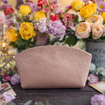 Blush pink floral-embossed leather makeup bag with a name, styled with a colorful bouquet