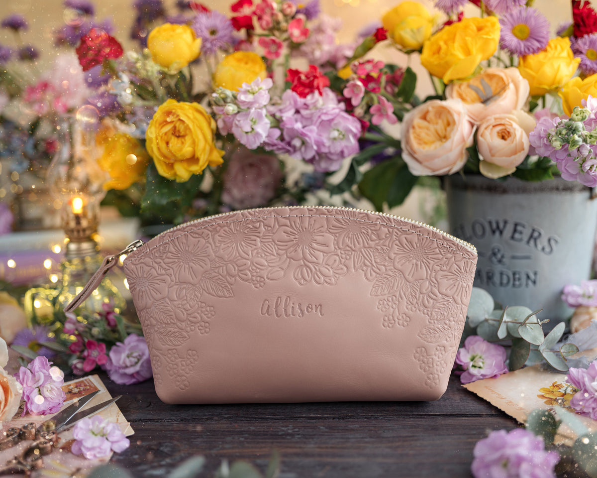 Blush pink floral-embossed leather makeup bag with a name, styled with a colorful bouquet