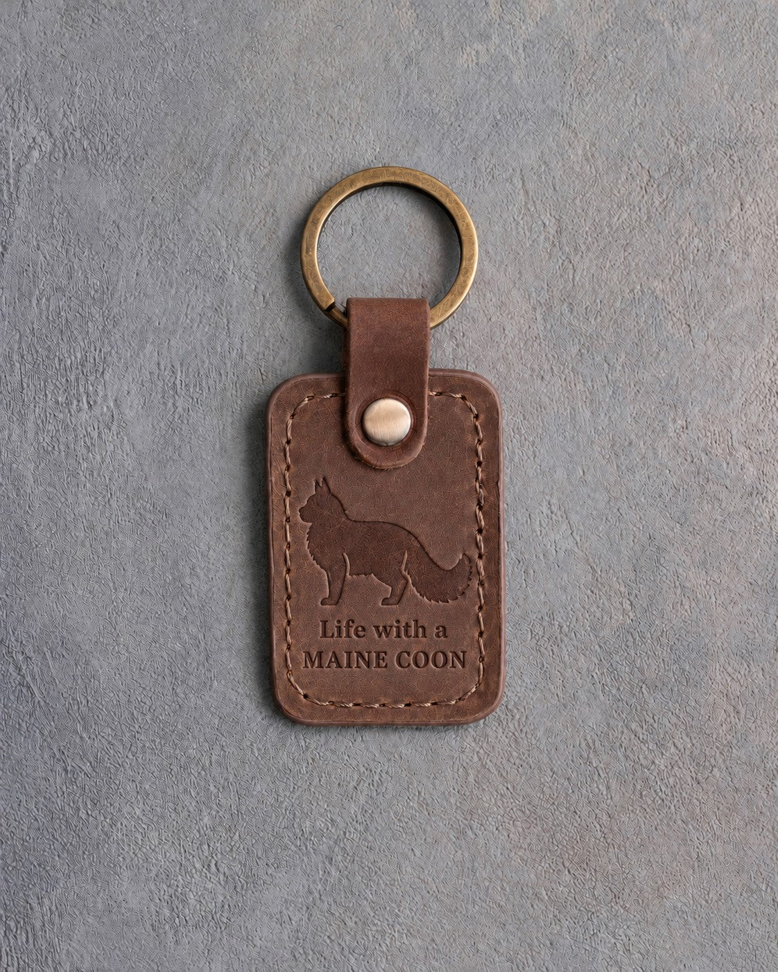 Sicilian brown leather keychain debossed with a standing Maine Coon cat above Life with a and MAINE COON, on gray concrete