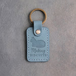 Turquoise leather keychain debossed with a loafing cat above the words Making BISCUITS
