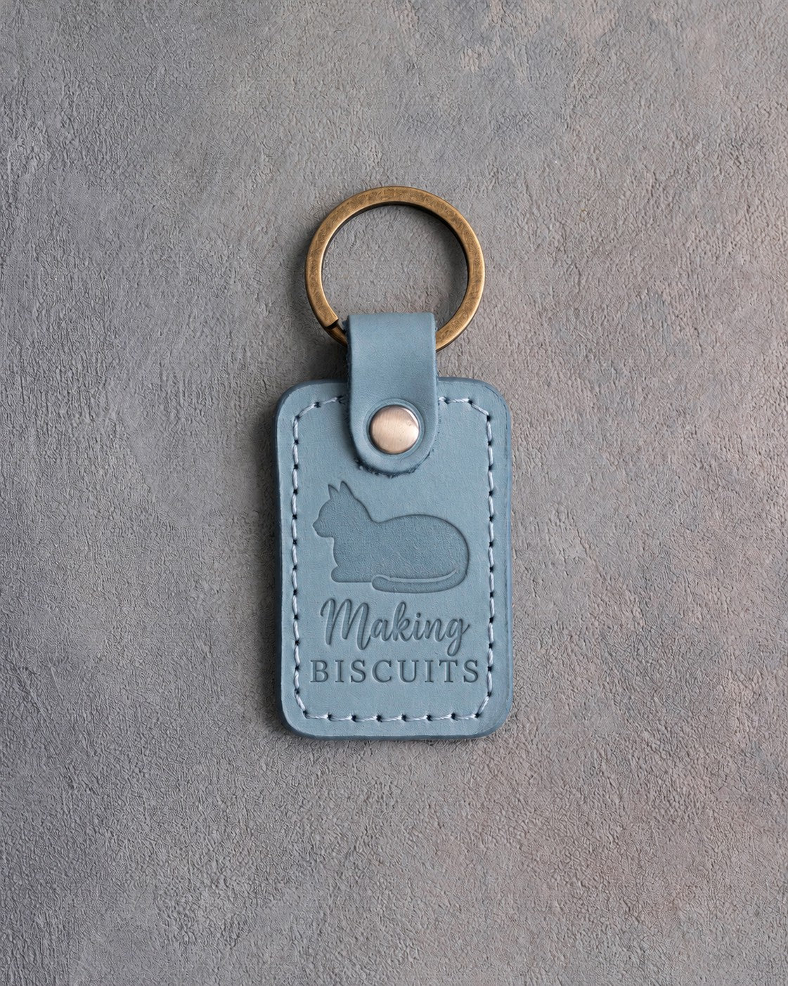 Turquoise leather keychain debossed with a loafing cat above the words Making BISCUITS