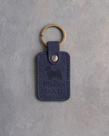 Blueberry navy leather keychain debossed with a Maltese silhouette and the words Maltese DAD, on gray concrete
