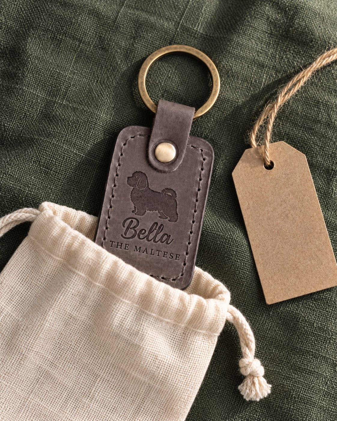 Country gray Bella the Maltese keychain held in a warm everyday setting