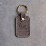 Country gray leather keychain debossed with a Maltese silhouette above THE MALTESE, on gray concrete