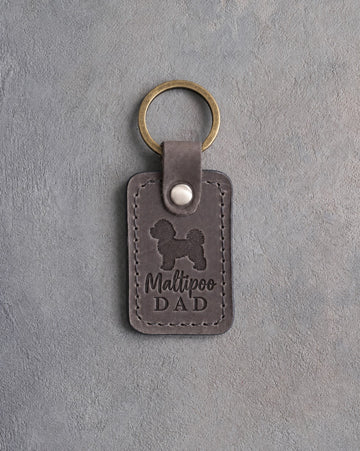 Country gray leather keychain debossed with a maltipoo silhouette and Maltipoo DAD, on gray concrete