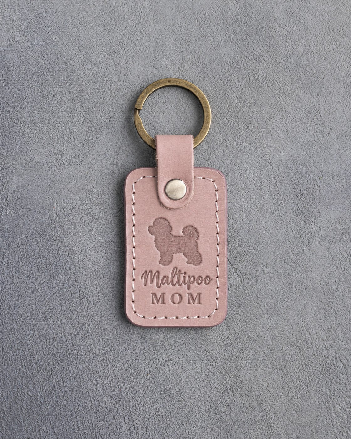 Blush pink leather keychain with a debossed maltipoo and the words Maltipoo MOM on gray concrete