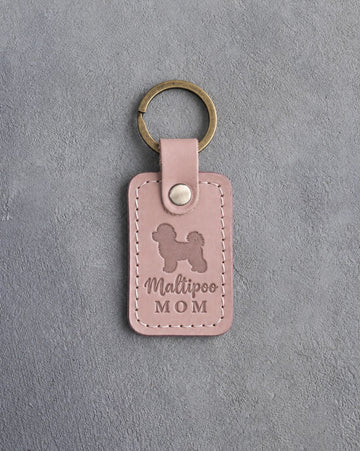 Blush pink leather keychain with a debossed maltipoo and the words Maltipoo MOM on gray concrete