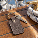 Country gray Marlin DAD keychain in full-grain leather on the worn teak cockpit table of a sailboat beside a coiled white dock line