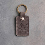 Country gray leather keychain debossed with a blue marlin above the words Marlin DAD, on gray plaster