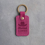 Fuchsia leather keychain debossed with a cowboy hat above Married and A COWBOY, on gray plaster