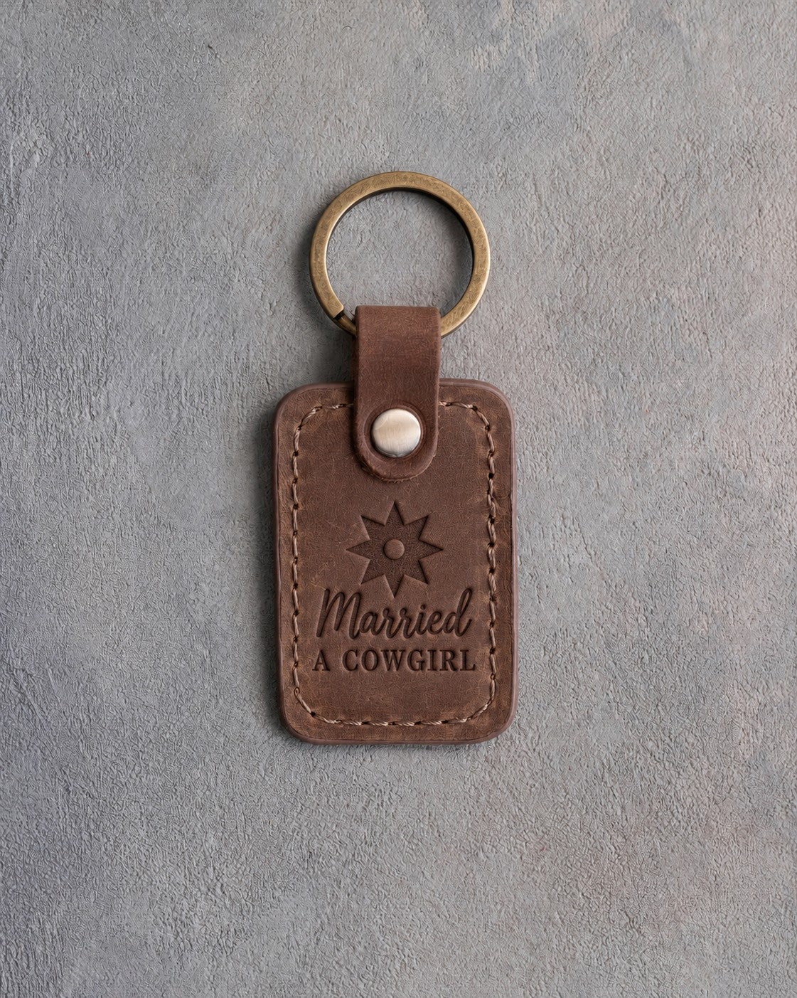 Sicilian brown leather keychain debossed with a spur rowel above Married and A COWGIRL, on gray plaster