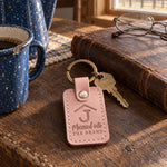 Blush Married into THE BRAND keychain on a dark oak ranch kitchen table beside a closed leather ledger