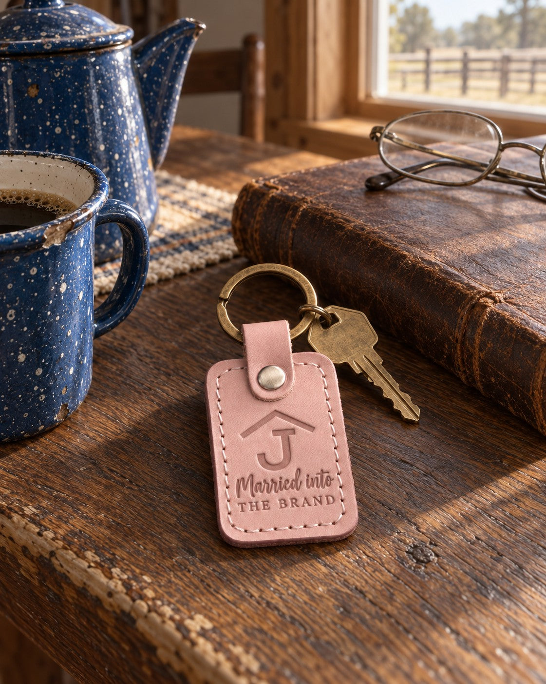 Blush Married into THE BRAND keychain on a dark oak ranch kitchen table beside a closed leather ledger