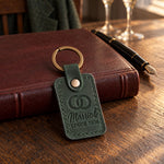 Married SINCE 2026 keychain in forest green leather on a dark oak table beside a closed register and a fountain pen