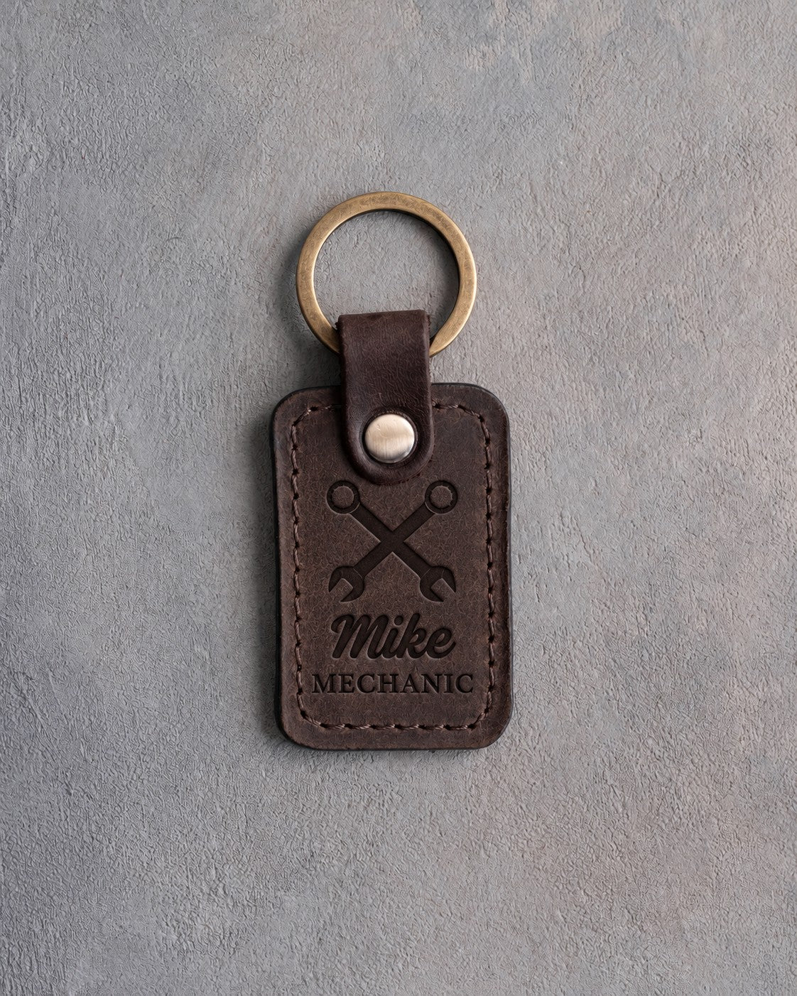 Dark espresso leather keychain debossed with two crossed wrenches above the name Mike and MECHANIC, on gray plaster