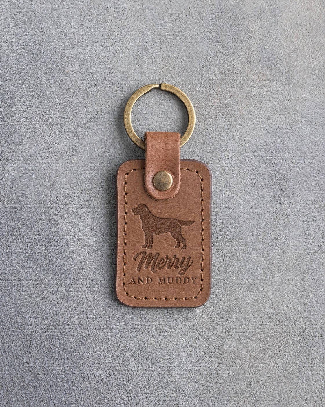 Caramel leather keychain debossed with a Labrador silhouette and the words Merry AND MUDDY, on gray concrete