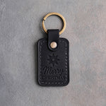 Black leather keychain with a gold foil spur rowel star above Merry and CHRISTMAS, on gray plaster