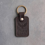 Dark espresso leather keychain debossed with an eagle in flight above the words Military DAD, on gray concrete