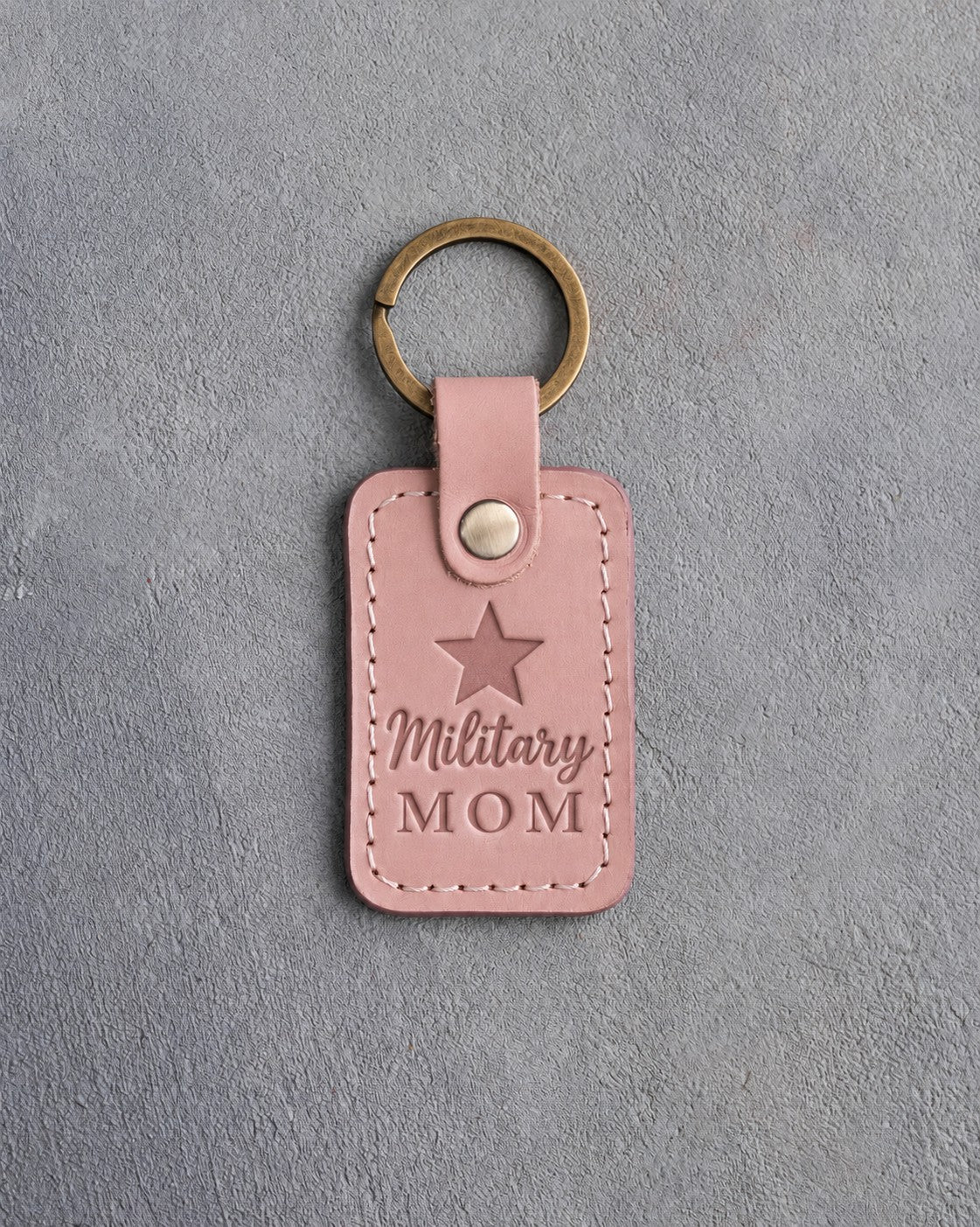 Blush pink leather keychain debossed with a five-point star above the words Military MOM, on gray concrete