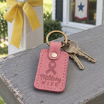 Pink Military Wife keychain on a house key beside a stack of moving boxes in a sunny hallway