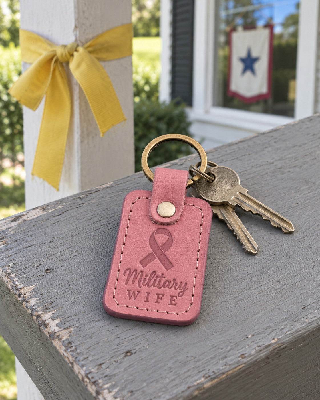 Pink Military Wife keychain on a house key beside a stack of moving boxes in a sunny hallway