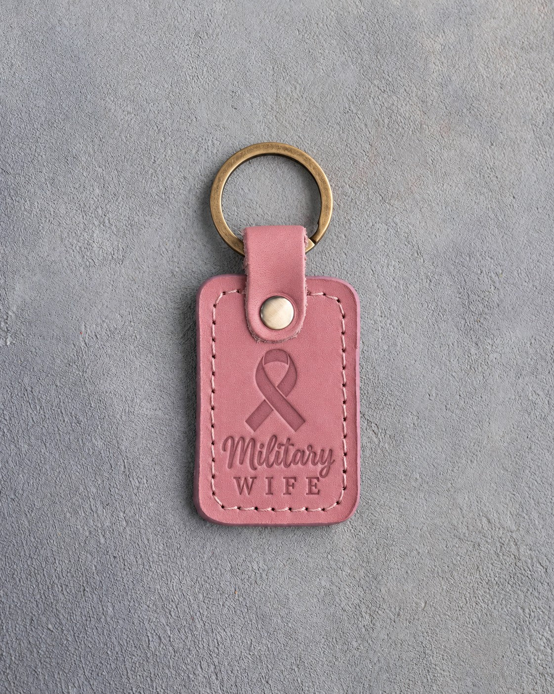 Rosy pink leather keychain debossed with a looped ribbon above the words Military WIFE, on gray concrete