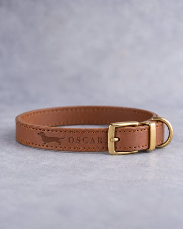 Slim caramel leather puppy collar with a miniature dachshund silhouette and the name OSCAR debossed, brass pin buckle