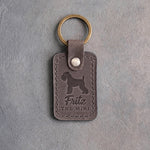Country gray leather keychain debossed with a Miniature Schnauzer silhouette, the name Fritz and THE MINI, on gray concrete
