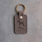 Country gray leather keychain debossed with a Miniature Schnauzer silhouette above Mini and SCHNAUZER, on gray concrete