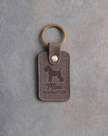 Country gray leather keychain debossed with a Miniature Schnauzer silhouette above Mini and SCHNAUZER, on gray concrete