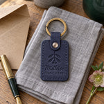 Navy Mistletoe Hang Here keychain on a front door key beneath a sprig of mistletoe tied with red ribbon