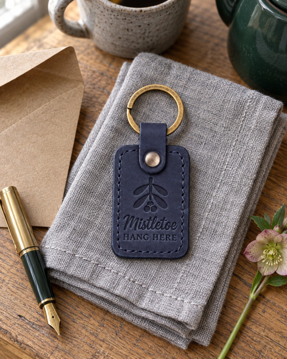 Navy Mistletoe Hang Here keychain on a front door key beneath a sprig of mistletoe tied with red ribbon