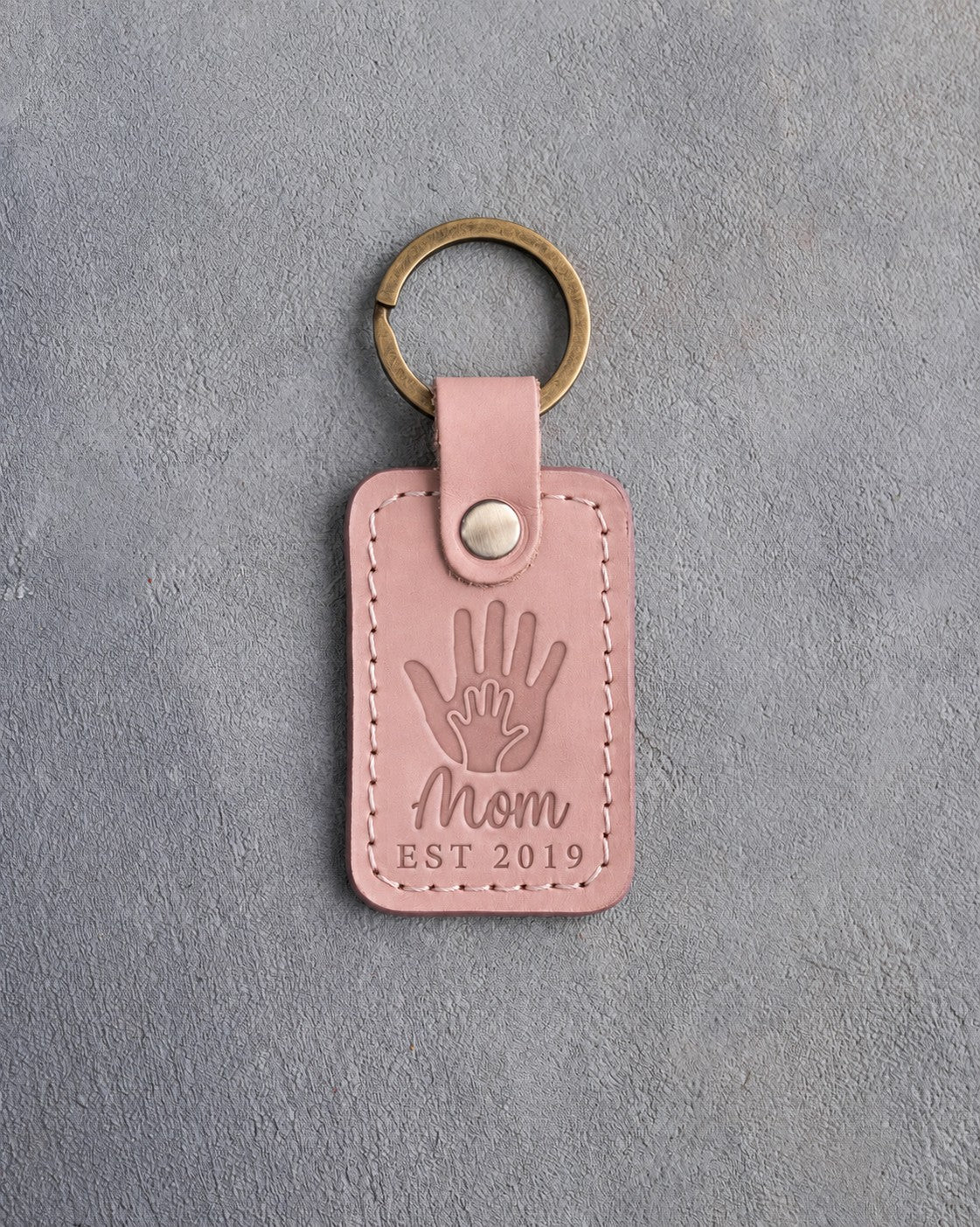 Blush pink leather keychain debossed with a small hand inside a large hand above Mom and EST 2019