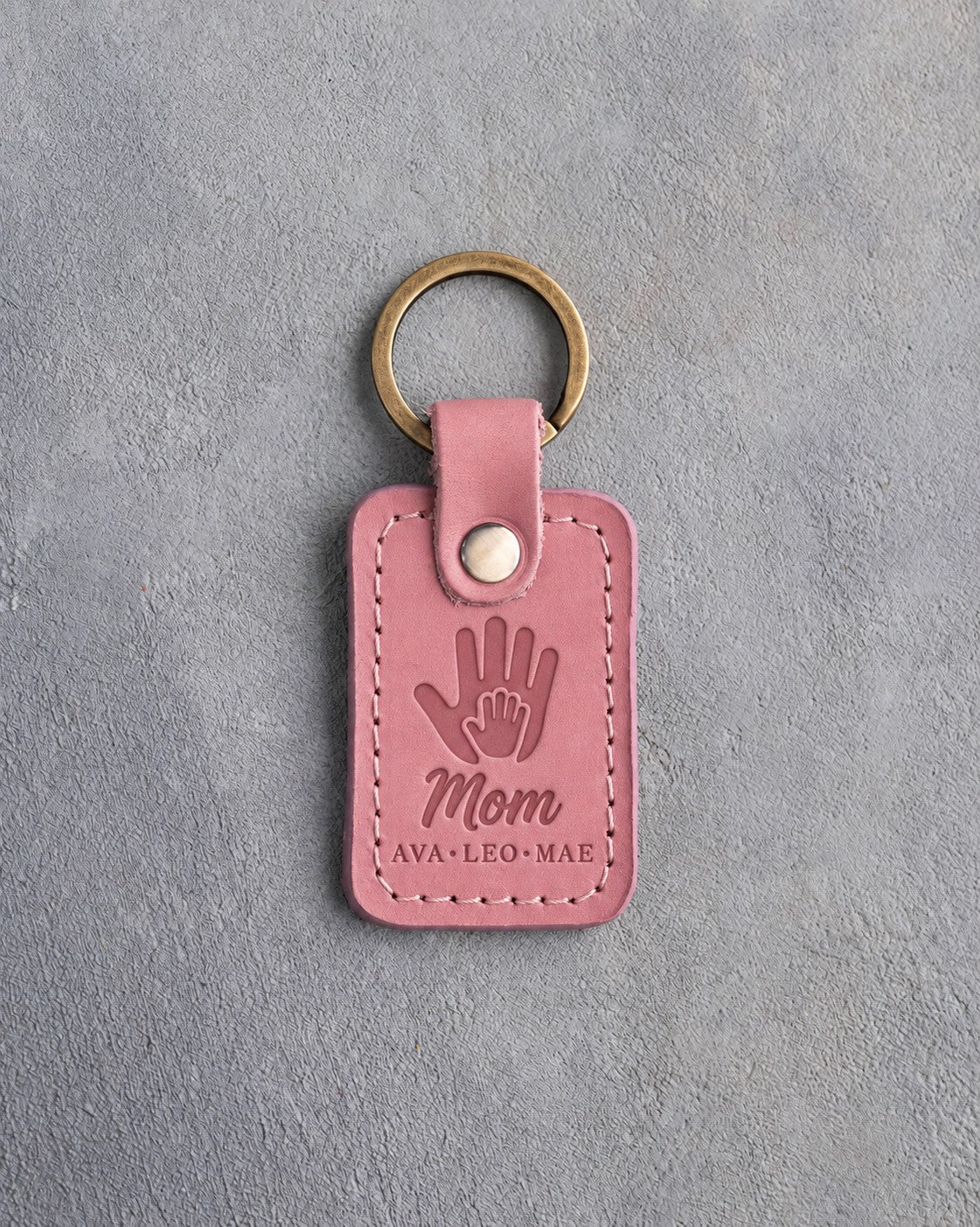 Parisian Blossom pink leather keychain debossed with a small hand inside a large hand above Mom and AVA·LEO·MAE