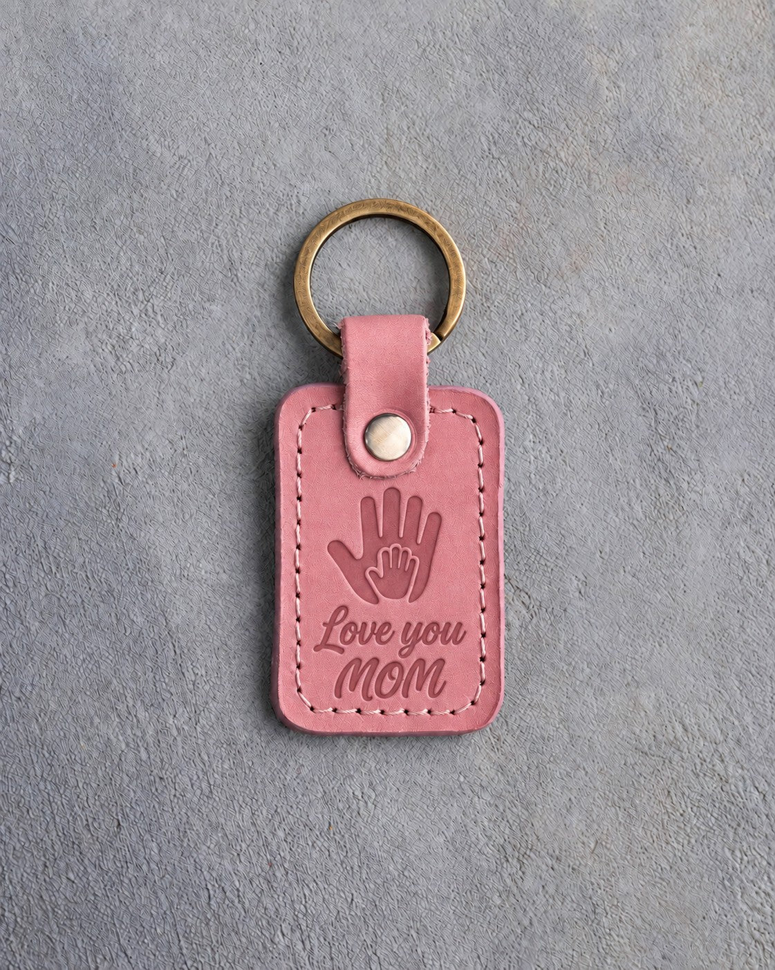 Parisian Blossom pink leather keychain debossed with a small hand inside a large hand above Love you and MOM, on gray concrete