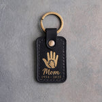 Black leather keychain with a gold foil small hand inside a large hand above Mom and 1954 · 2025