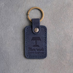 Blueberry navy leather keychain debossed with a banker's lamp above Mom reads and AFTER BEDTIME, on gray concrete