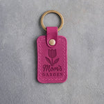 Fuchsia leather keychain debossed with a tulip above Mom's GARDEN, on gray concrete