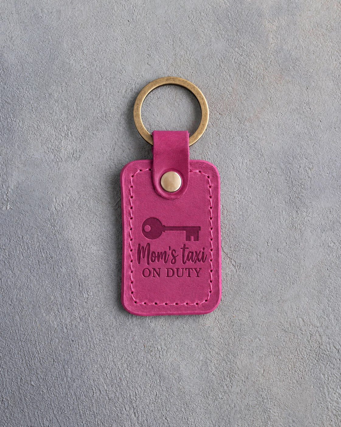 Fuchsia leather keychain debossed with an old key below Mom's taxi and ON DUTY