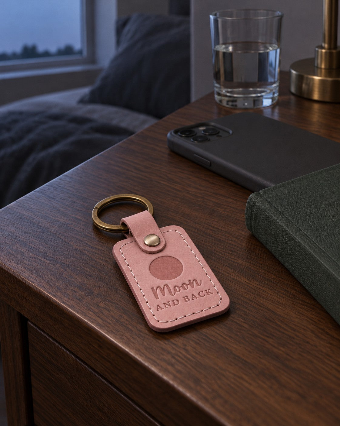 Pink Moon and Back keychain resting on a folded baby blanket beside a set of car keys in soft morning light