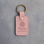 Blush pink leather keychain debossed with a solid full moon above the words Moon AND BACK, on gray concrete