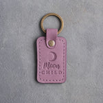 Lilac leather keychain debossed with a waxing crescent moon above the words Moon CHILD, on gray concrete
