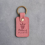 Parisian blossom pink leather keychain debossed with a potted plant above Mother of PLANTS, on gray concrete