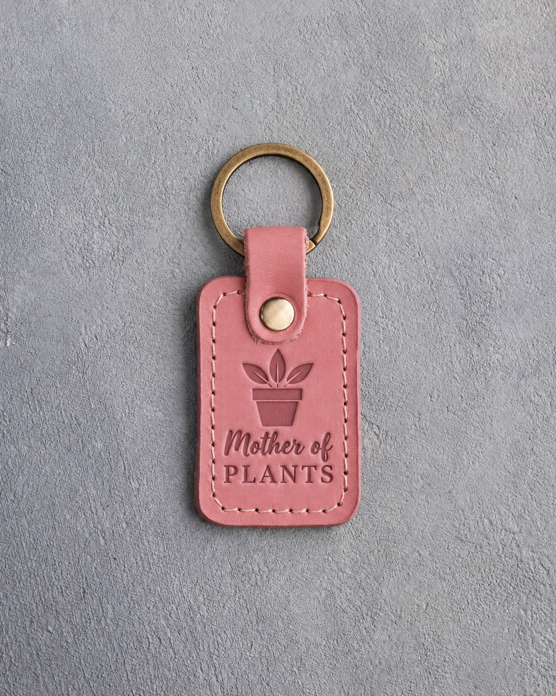 Parisian blossom pink leather keychain debossed with a potted plant above Mother of PLANTS, on gray concrete