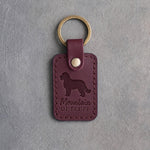 Sangria red leather keychain debossed with a Bernedoodle silhouette and the words Mountain OF FLUFF, on gray concrete