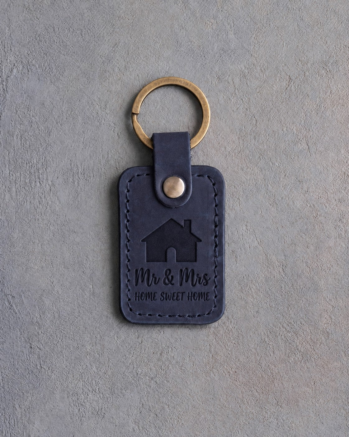 Blueberry navy leather keychain debossed with a gabled house above Mr & Mrs and HOME SWEET HOME, on gray concrete