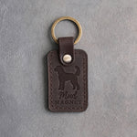 Dark espresso leather keychain debossed with a goldendoodle silhouette and the words Mud MAGNET, on gray concrete
