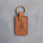 Caramel leather keychain debossed with a pyramid metronome above the words Thank you and MUSIC TEACHER, on gray concrete