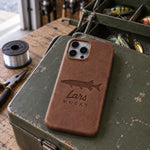 Sicilian Brown Lars MUSKY iPhone case in full-grain leather on the lid of an olive-green steel tackle box in a garage, lures in the trays behind