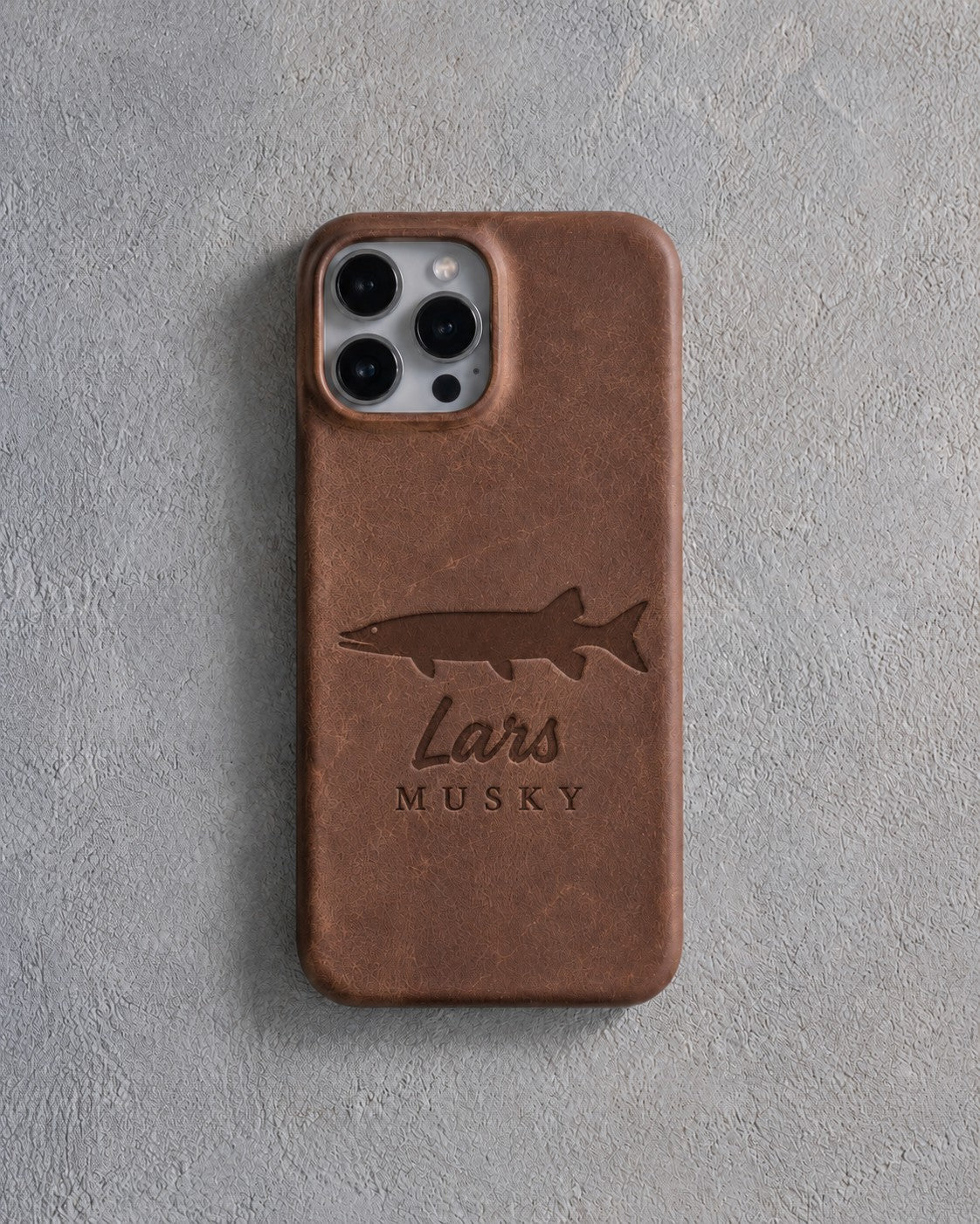 Back of a sicilian brown leather iPhone case debossed with a musky above Lars and MUSKY below the camera, on gray plaster